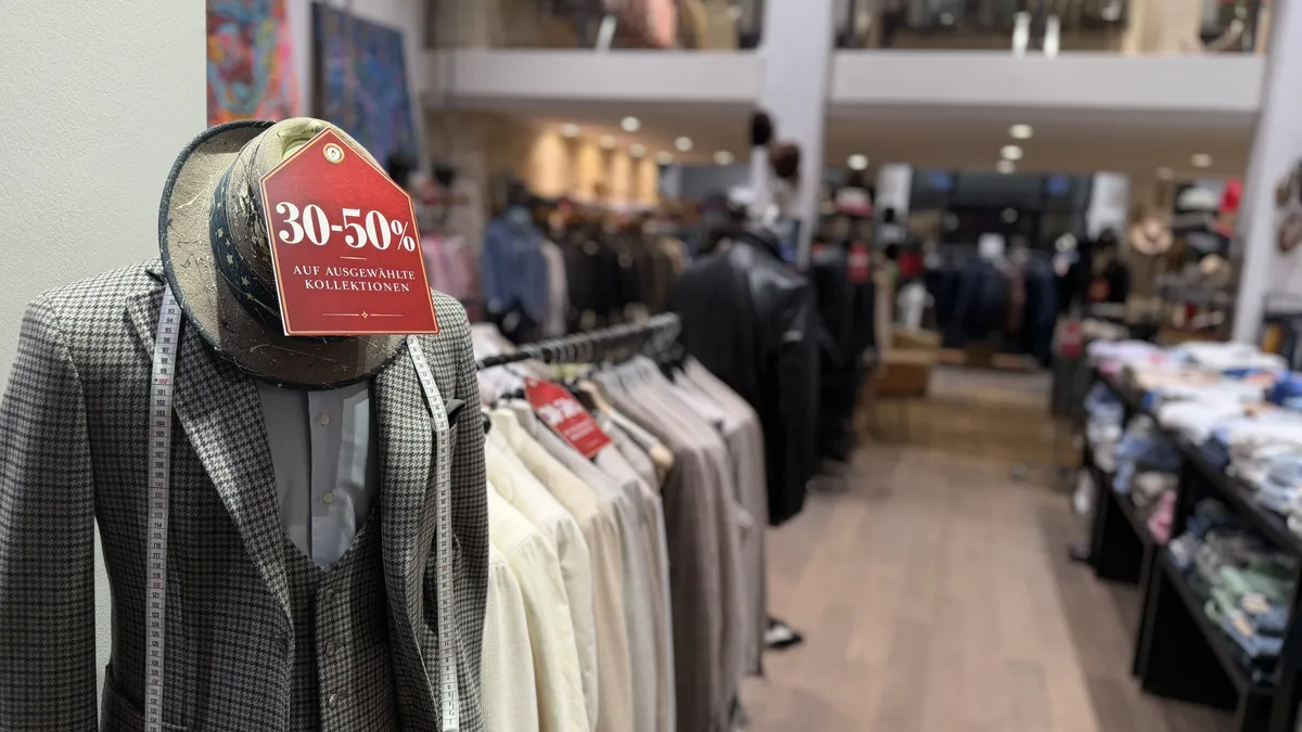 Büste mit Hahnentritt-Sakko, Weste, Hut und Maßband – Schild „30–50 % auf ausgewählte Kollektionen“
