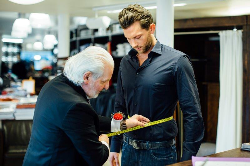 Schneider nimmt mit gelbem Maßband an einem Kunden Maß – Anpassung in der LO&GO-Schneiderei
